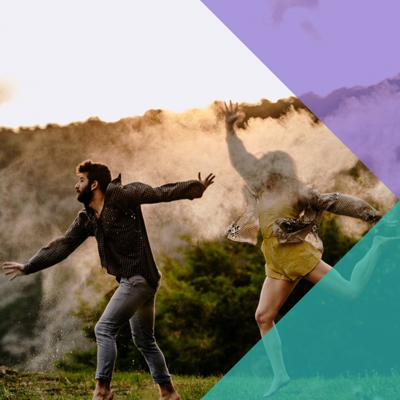 Two people dancing outside on a grassy field with a misty treelined hill in the background